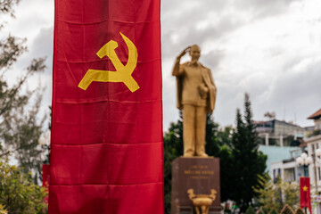 A communist flag with hammer and sickle displayed in front of a statue of Ho Chi Minh in Vietnam.