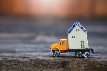 House model on orange truck over blurred background, house move, property and transportation business concept