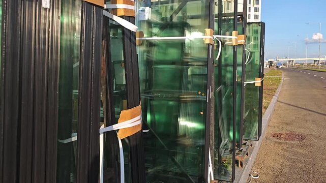 Facade glass is stacked near the construction site, high-rise buildings are clad with facade glass, windows are installed, and glass is stored outdoors and ready for installation
