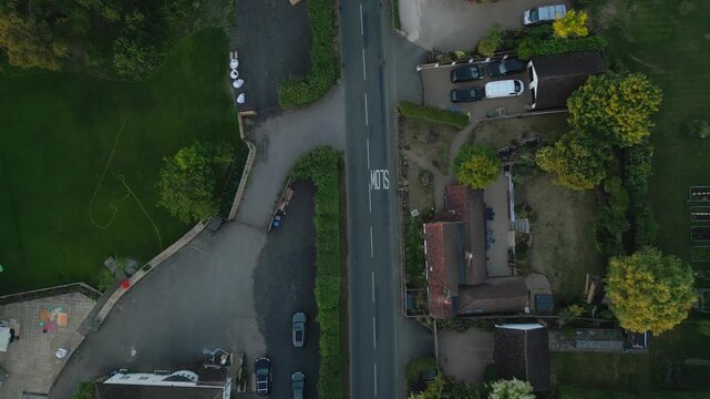 Aerial view of a rural road, houses, parked cars, and green lawns. 
SLOW marking is visible on the road.