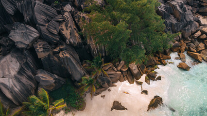Tropical beach with large granite rocks, palm trees, and turquoise water on white sand shoreline