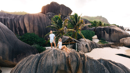 Couple on large rocks by tropical beach with palm trees during vacation