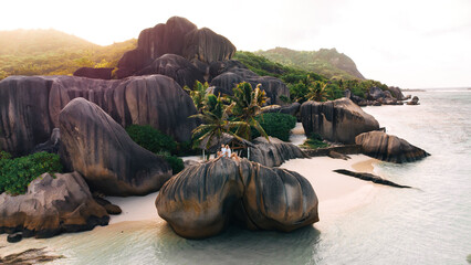 Couple relaxing on granite rocks along a tropical beach at sunset with palm trees and clear water