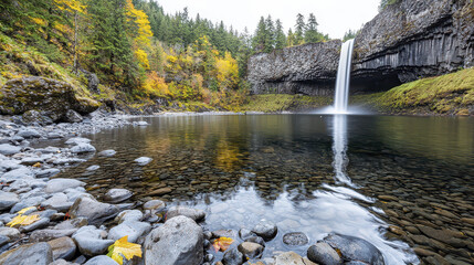 Serene landscape featuring waterfall cascading into tranquil pool surrounded by autumn foliage and rocky terrain