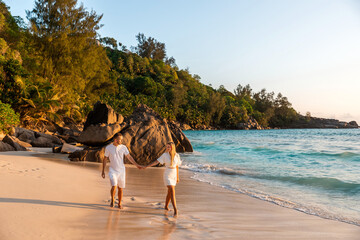 Honeymoon romantic couple in love holding hands walking on beautiful sunset at beach in waterfront. Lovers or newlywed married young couple by the sea enjoying relaxed vacation travel holiday. Hawaii.