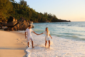 Beach couple walking on romantic travel honeymoon vacation summer holidays romance. Young happy lovers, woman and man holding hands.