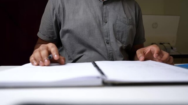 Person writing in a notebook at a desk, focus on hands