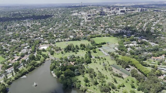 Drone flies backwards hgh over Zoo Lake on sunny day in Randburg, Johannesburg, South Africa