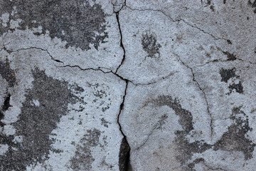 Old cement or plaster wall surface with a large Y-shaped crack in the center and mottled patches. Abstract grunge background illustrating damage and decay