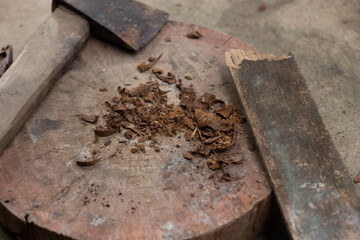 Old axe/knife and shaved wood pieces placed on a round wooden cutting board. Illustrates tools, manual labor, traditional food preparation, or a rustic setting