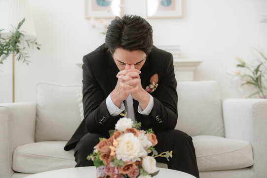 Stressed groom sitting on sofa with hands on head before wedding.