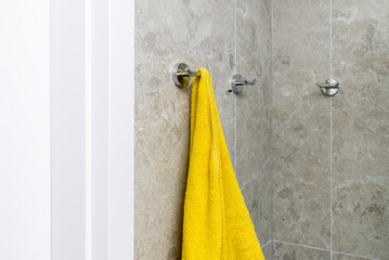 Fototapeta premium Bathroom with gray stone tile walls and chrome towel hooks. a yellow towel is hanging.
