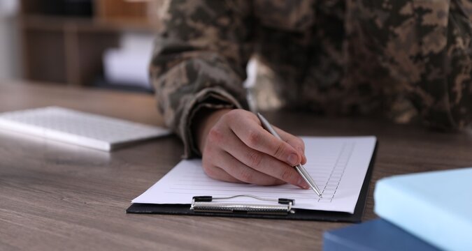 Military education. Student in soldier uniform learning at wooden desk indoors, closeup. Space for text
