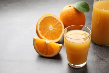 Fresh orange juice and fruits on grey table, closeup. Space for text