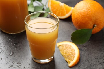 Fresh orange juice, fruits and leaves on grey table, closeup