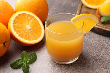 Fresh orange juice in glass, mint and fruits on grey table, closeup