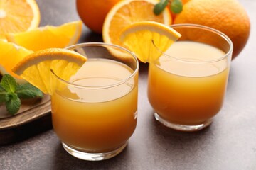 Fresh orange juice in glasses, mint and fruits on grey table, closeup