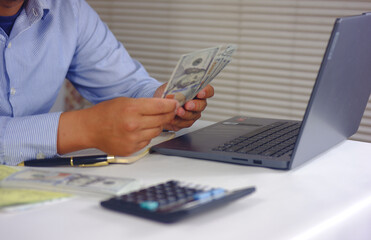 Financial planning, Home finances, budget, savings and spends concept. Counting cash dollars in front of a laptop and plotting them into several sections. Financial management concepts.
