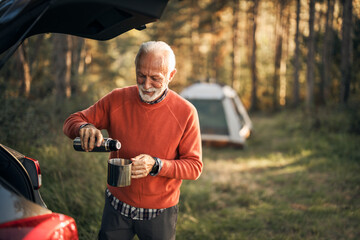 Senior Man Camping in Forest Enjoying Morning Coffee Near Tent and SUV