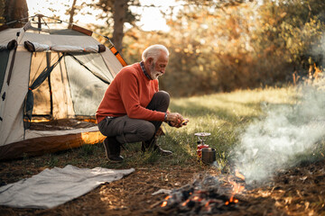Senior Camper Cooking by a Campfire Near Forest Tent