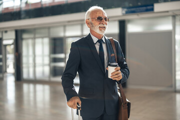 Confident Senior Businessman at Airport with Coffee and Suitcase