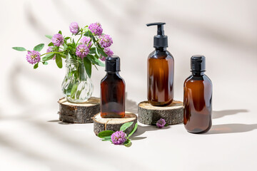 Skin care products in amber bottles next to pink clover flowers on a beige background. The concept of natural cosmetics