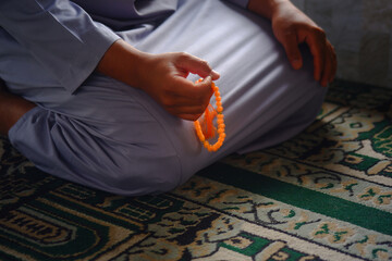 Close-up of hands reciting dhikr using prayer beads against a blurred background. Hands reciting dhikr. A man reciting dhikr while holding a prayer beads. A Muslim's worship activity.
