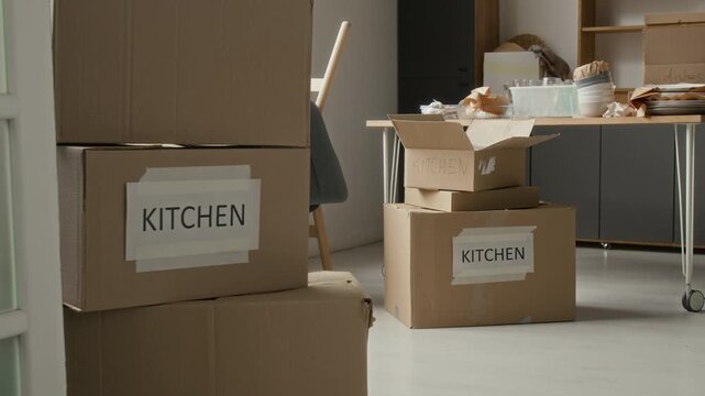 No people shot of room with cardboard boxes labeled kitchen and dining table on wheels cluttered with dishes in background