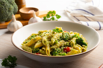 Vegetarian vegan green pasta, Penne pasta with pesto sauce with sliced broccoli and tomato in white plate.Topped with vegan cheese in white plate.Healthy food.