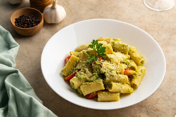 Vegetarian vegan green pasta, Rigatoni pasta with broccoli pesto sauce and tomato.Topped with vegan cheese in white plate.Healthy food.