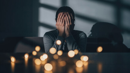 Man covering face with hands while sitting in dark room with lights  