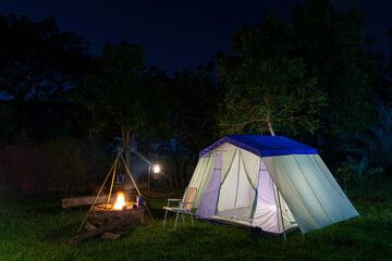 Nighttime camping tent in a forest clearing surrounded by nature