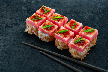 Elegant tuna sushi rolls topped with fresh raw tuna, teriyaki glaze, and green onions, served with chopsticks on dark slate. Luxury Japanese maki, gourmet tuna roll, premium seafood sushi.