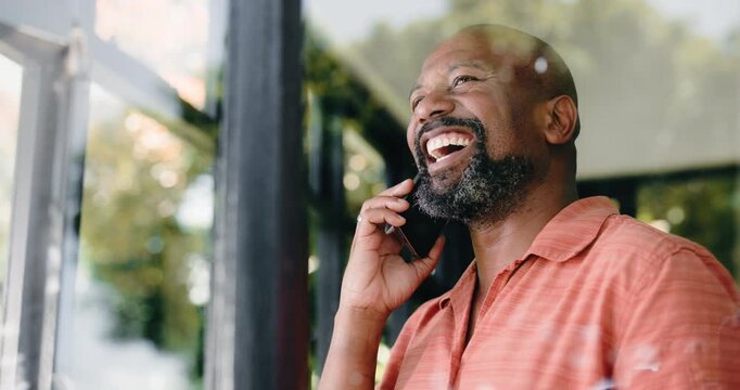 Laugh, black man and phone call in home for talking to contact, news or joke with low angle. Mobile, chat and mature person with funny story for humor, conversation or bye for communication by window