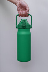 A hand holds a large, textured green insulated water bottle with a convenient handle and straw lid. 