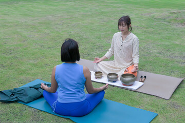 Woman performing sound healing with Tibetan singing bowls during relaxation yoga session outdoors.