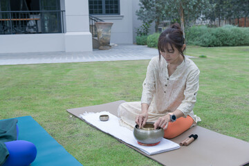 Woman performing sound healing with Tibetan singing bowls during relaxation yoga session outdoors.