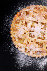 A half of apple pie sprinkled with powdered sugar on black background