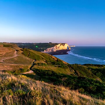 Coastal sunset view; bluffs overlooking the ocean. Rolling grassy hills lead to a scenic seascape under a clear blue sky
