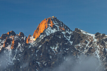 Lomnicky peak in High Tatras National Park, Slovakia, Europe. Golden hour bathes a majestic, snow-dusted mountain peak under clear blue skies, a serene and captivating alpine vista.