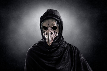 Creepy figure with animal bird skull over dark misty background