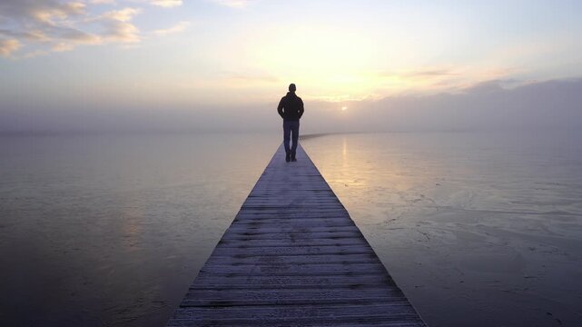 A man walking on a jetty (Knuppelpad) in nature reserve Roegwold during a cold, foggy sunrise.