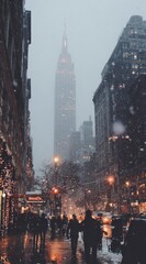Obraz premium A city street scene under a snowy evening, featuring the Empire State Building in the background, with warm holiday lights illuminating the dark silhouettes of pedestrians.