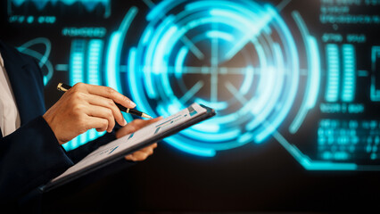 A business professional woman hands reviews data on clipboard while holding pen, standing before futuristic digital interface with glowing blue analytics, emphasizing technology-driven analysis.
