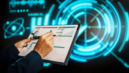 A business professional woman hands reviews data on clipboard while holding pen, standing before futuristic digital interface with glowing blue analytics, emphasizing technology-driven analysis.