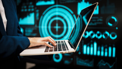 Professional working on laptop in front of futuristic digital dashboards, highlighting data analytics, cybersecurity insights, real-time visual information that reflect modern technology.
