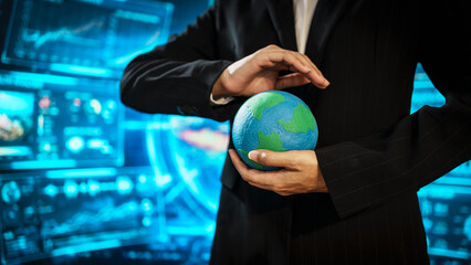 Business professional holding small Earth model before futuristic digital interface, global...