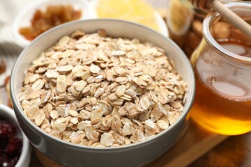 Making granola. Oat flakes in bowl and honey on table, closeup
