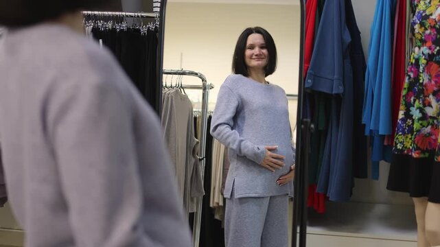 Pregnant woman. Touching her belly. Clothing store. Slow motion video. High-quality 4K footage.