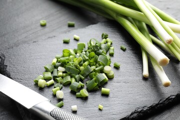 Fresh green onions and knife on black table, closeup